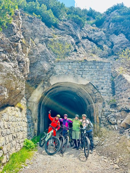 E-MTB Camp Gardasee 2026 Fünf E-MTB-Fahrerinnen stehen mit ihren Bikes in einem historischen Felsentunnel am Tremalzopass oberhalb des Gardasees.