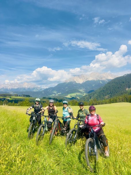 E-MTB Camp Dolomiti 2026 Sechs E-MTB-Fahrerinnen stehen mit ihren Bikes auf einer Almwiese vor dem Bergpanorama der Dolomiten.