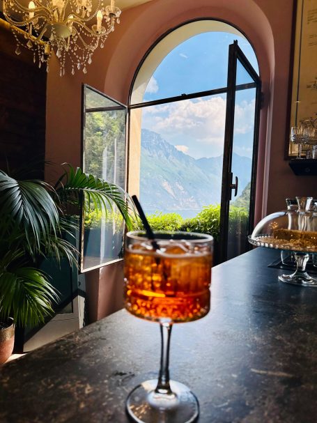 E-MTB Camp Gardasee 2026 Aperol Spritz auf einem Tresen am offenen Fenster im Ponale Alto Belvedere mit Blick auf den Gardasee und die Berge.