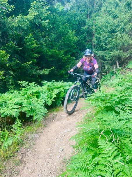 E-MTB Camp Ultental 2026 E-MTB-Fahrerin fährt auf einem schmalen Waldtrail durch hohe Farne beim Frauen-Camp im Ultental in Südtirol.